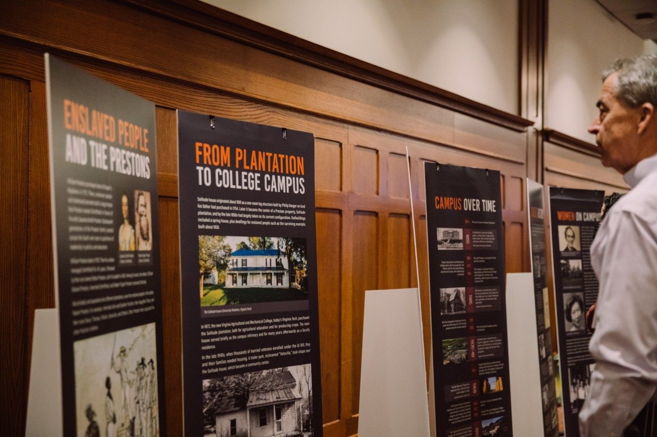 A man looks at a display of historic facts presented on tall, standing signs. One sign is titled Enslaved People and the Prestons. The other sign is From Plantation to College Campus.